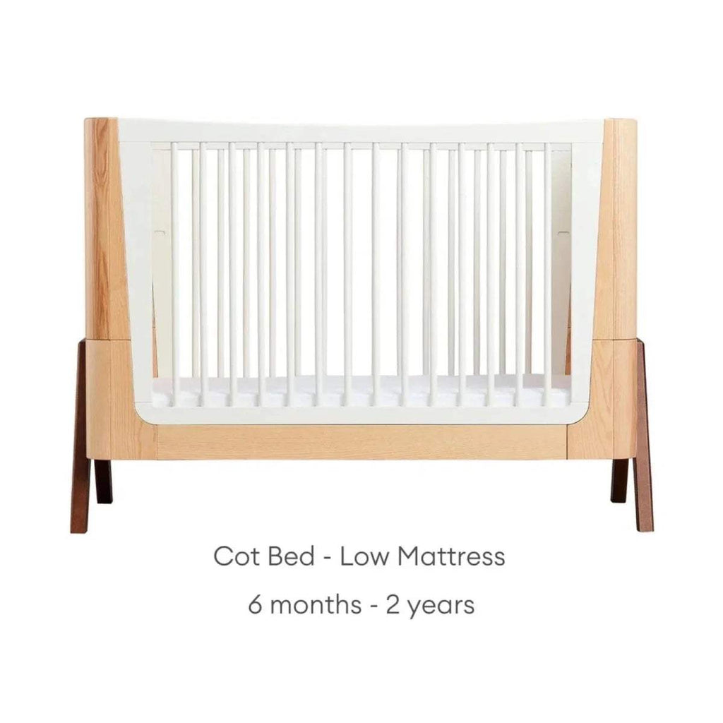 Convertible cot bed with natural wood frame and white slat sides; low-height white mattress