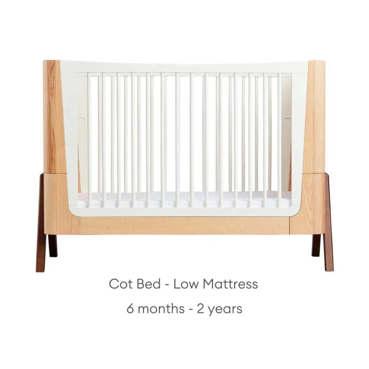 Convertible cot bed with natural wood frame and white slat sides; low-height white mattress