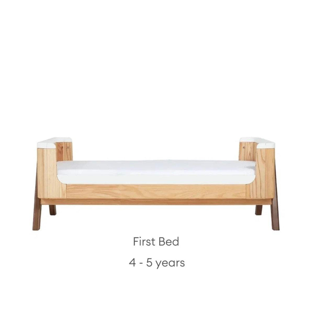 Convertible first bed with natural wood sides and white guard rail; low bed height