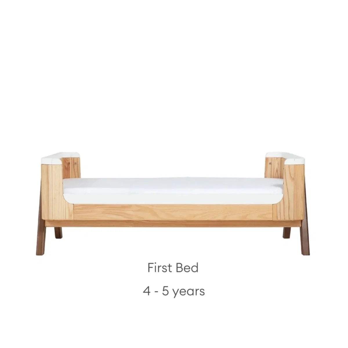 Convertible first bed with natural wood sides and white guard rail; low bed height