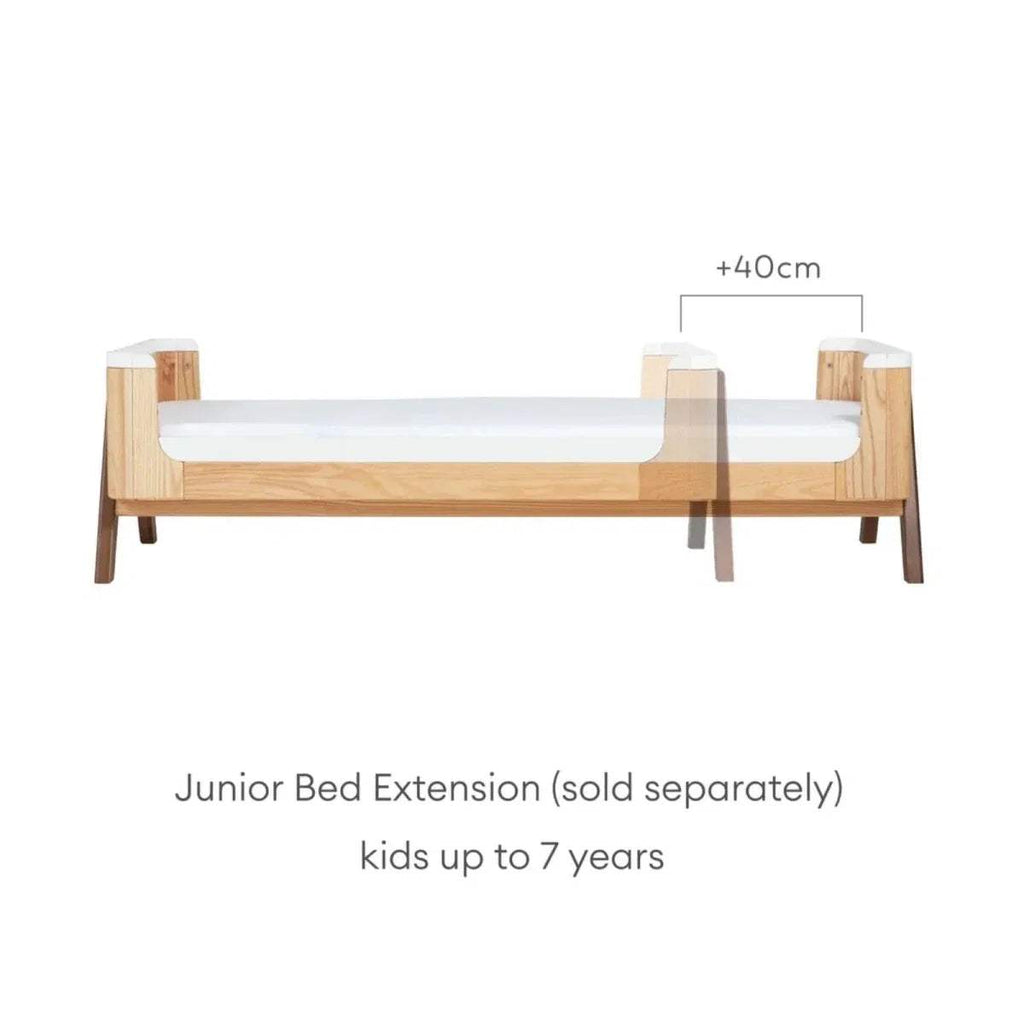 Convertible junior bed with natural wood frame, white side rails, and longer extended length