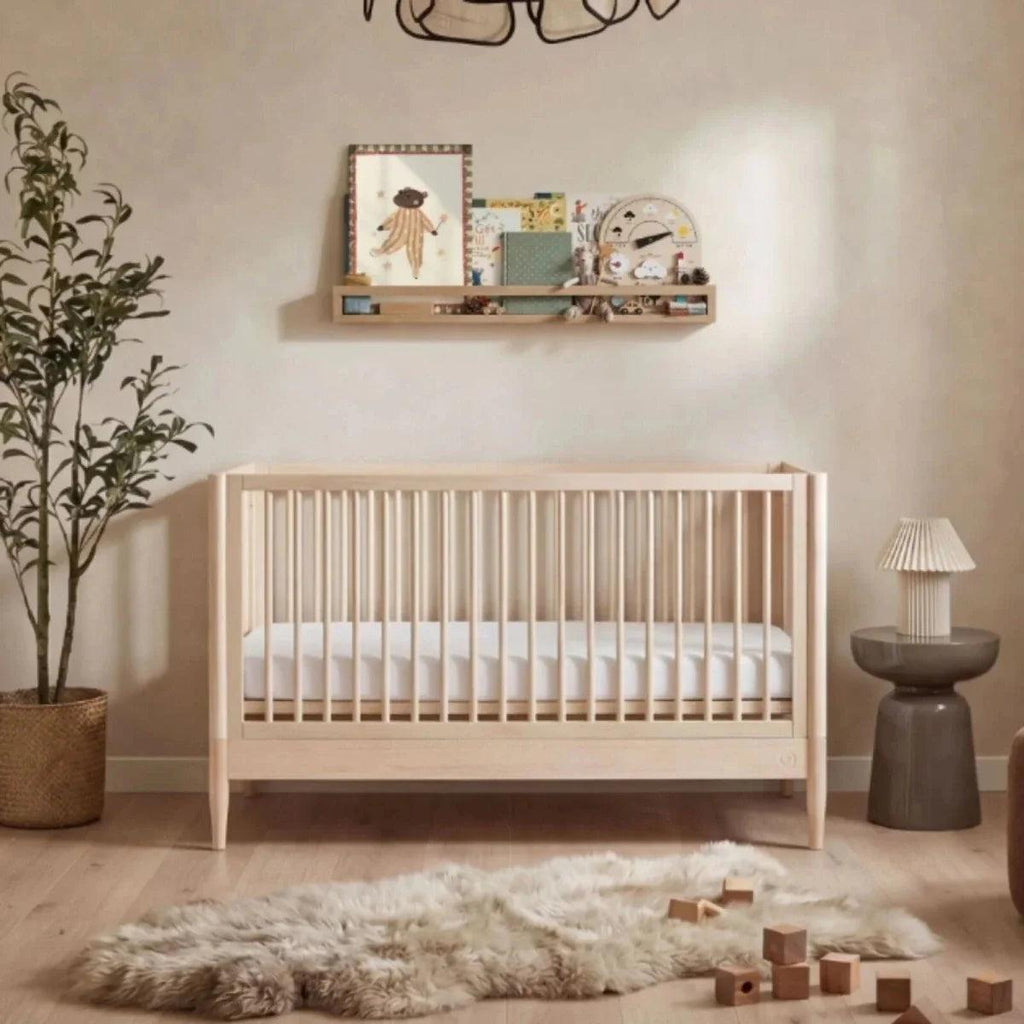 Natural ash baby crib with white mattress and tall vertical slat guard