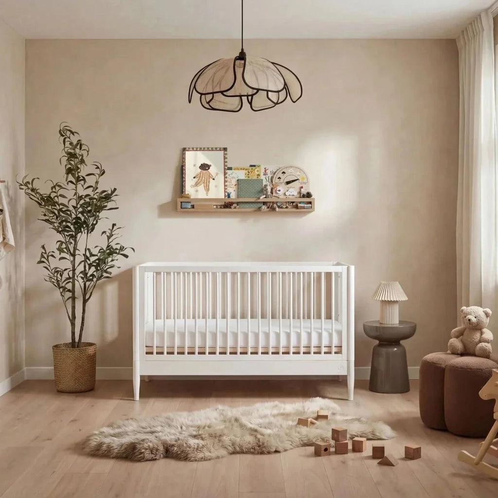 All-white nursery room set with white crib, bedside lamp, and teddy chair