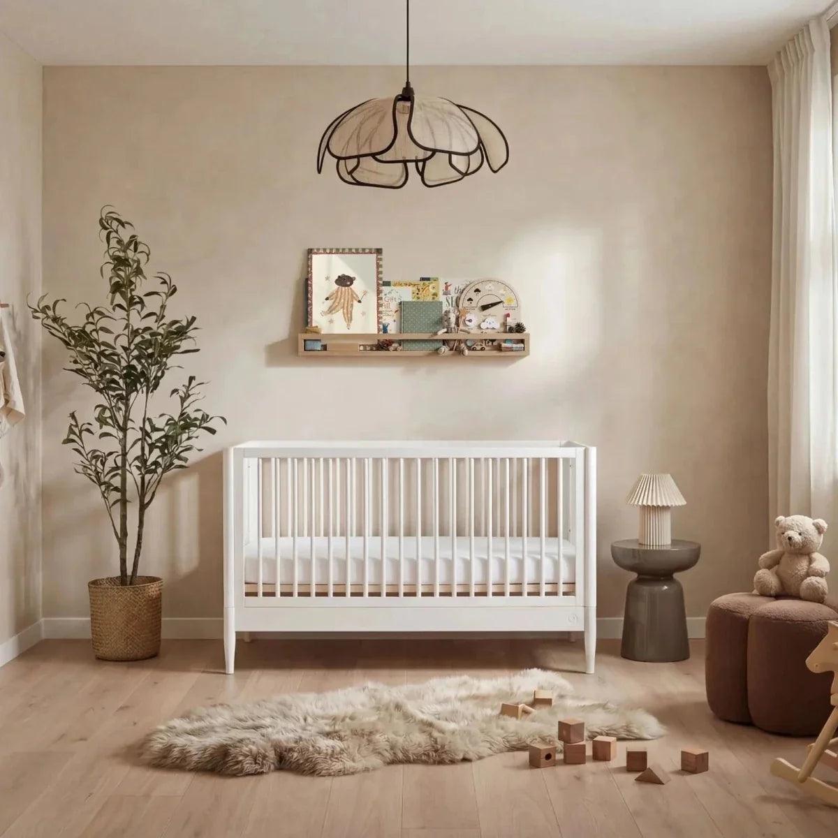 All-white nursery room set with white crib, bedside lamp, and teddy chair