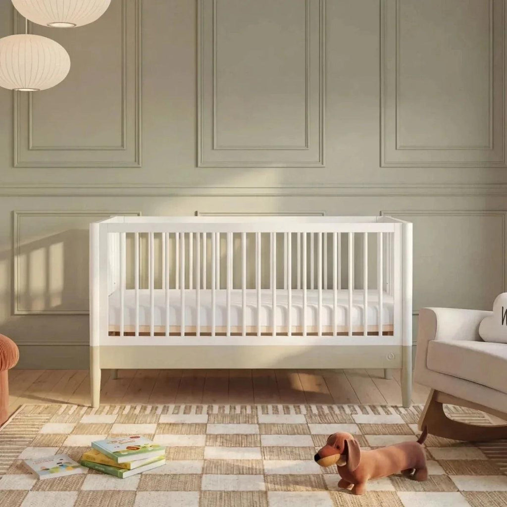 White baby crib with slatted sides and desert sage accent rail, shown in a nursery