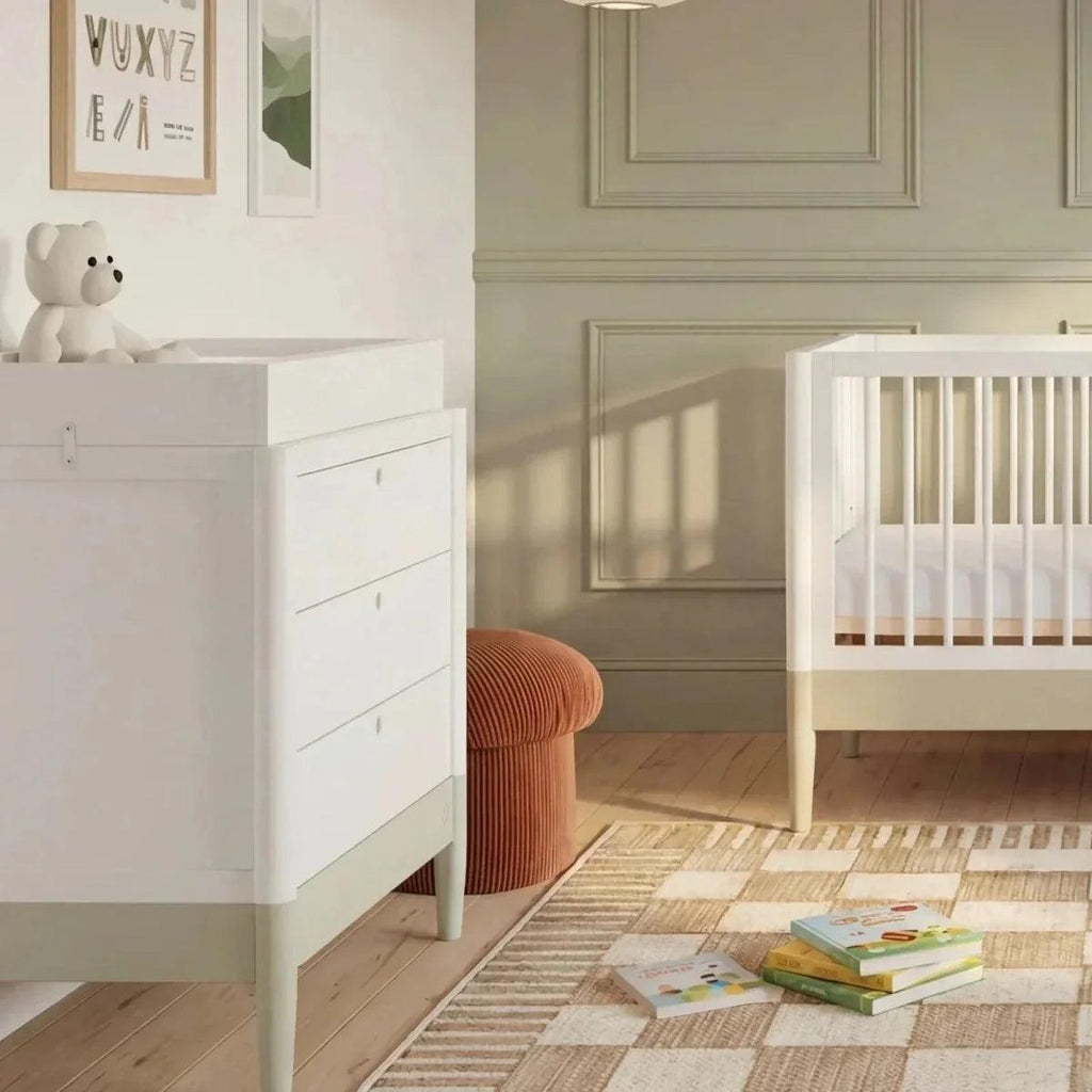 White baby crib next to a white dresser-style changing unit, desert sage accents