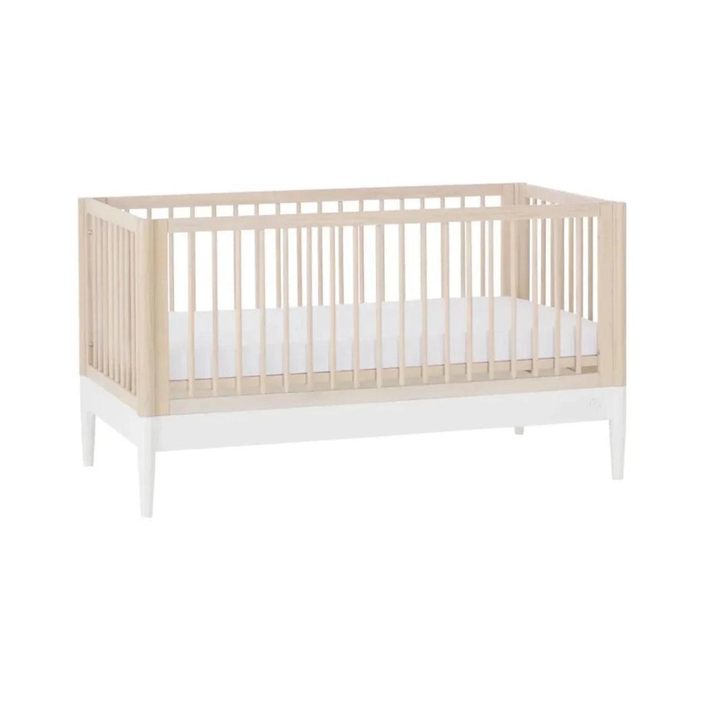 Wooden baby crib with natural ash frame, white slatted sides, and mattress base