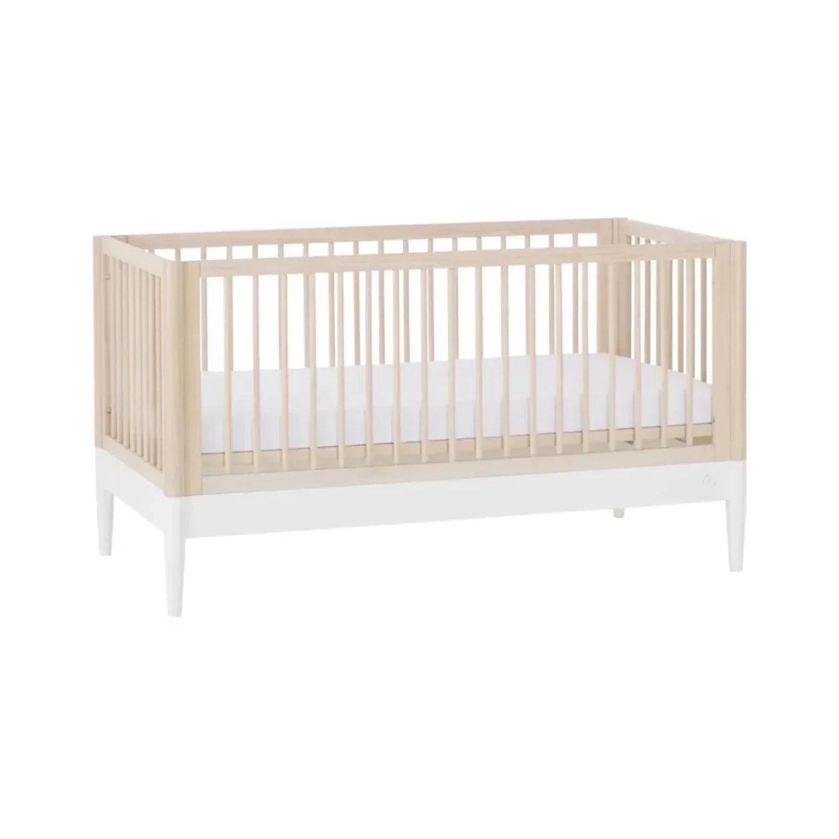 Wooden baby crib with natural ash frame, white slatted sides, and mattress base