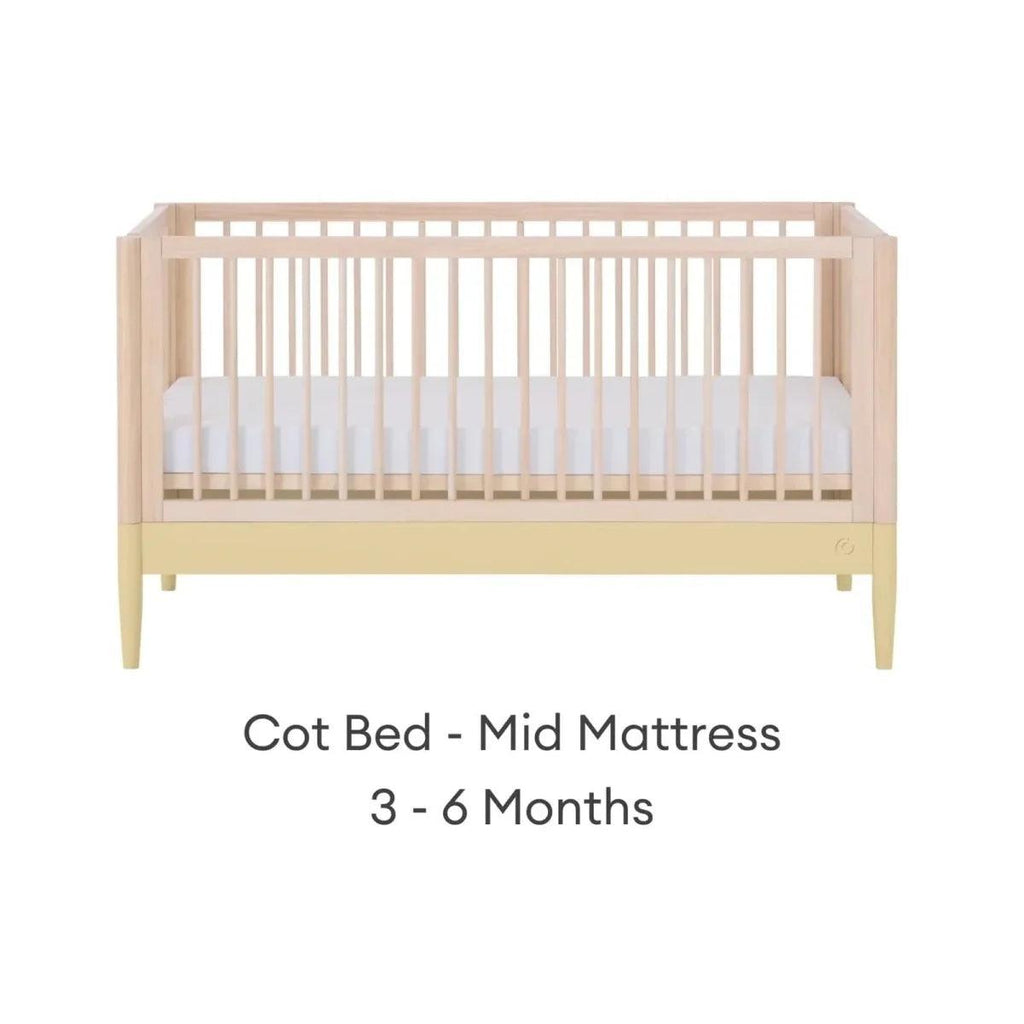 Cot bed with mid mattress level, light wood frame and white mattress panel