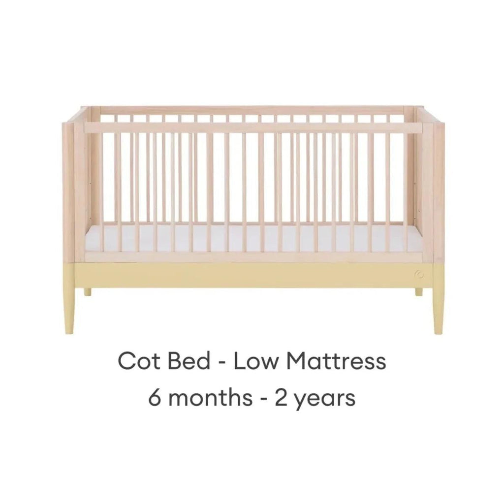 Cot bed with low mattress level, light wood frame and white mattress panel