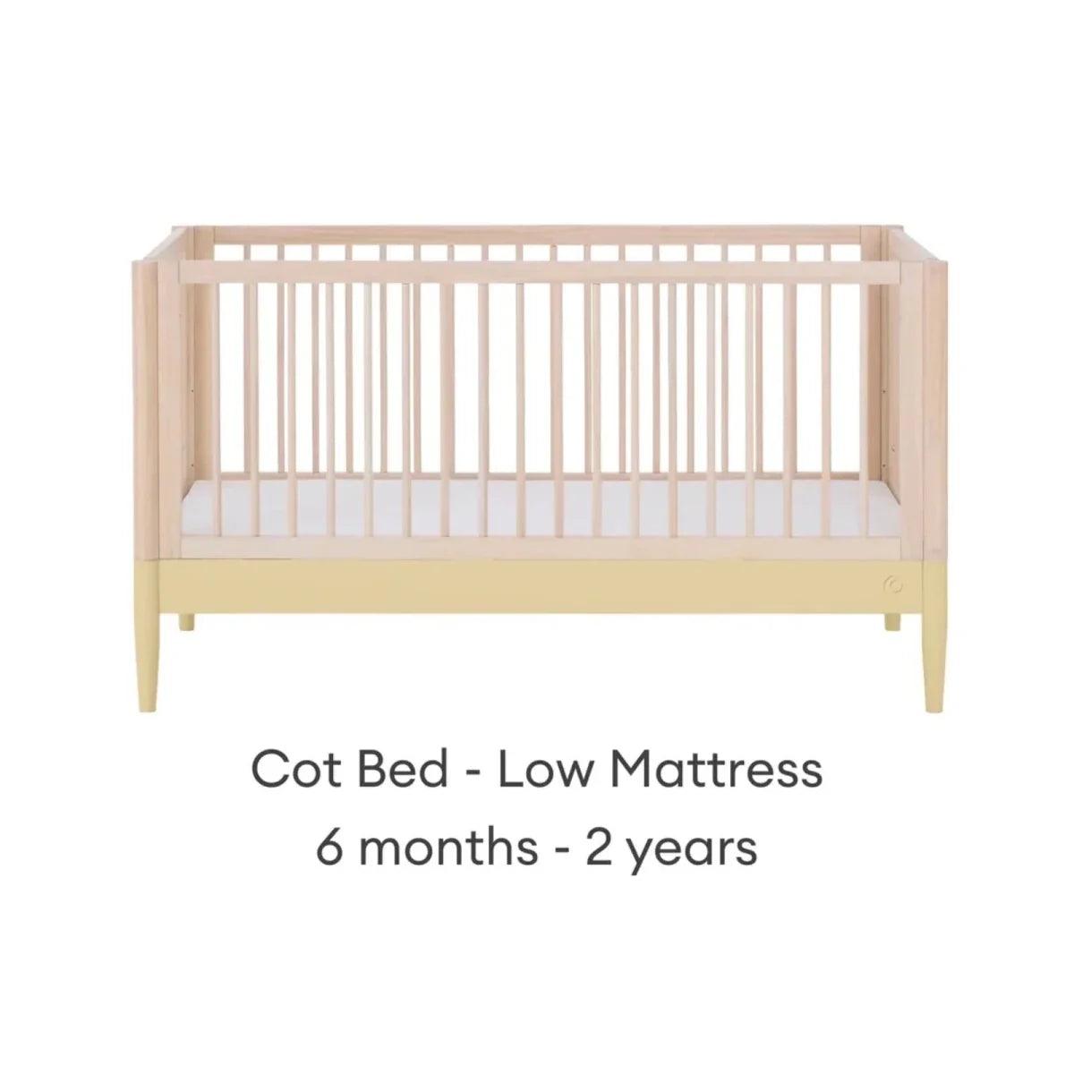 Cot bed with low mattress level, light wood frame and white mattress panel