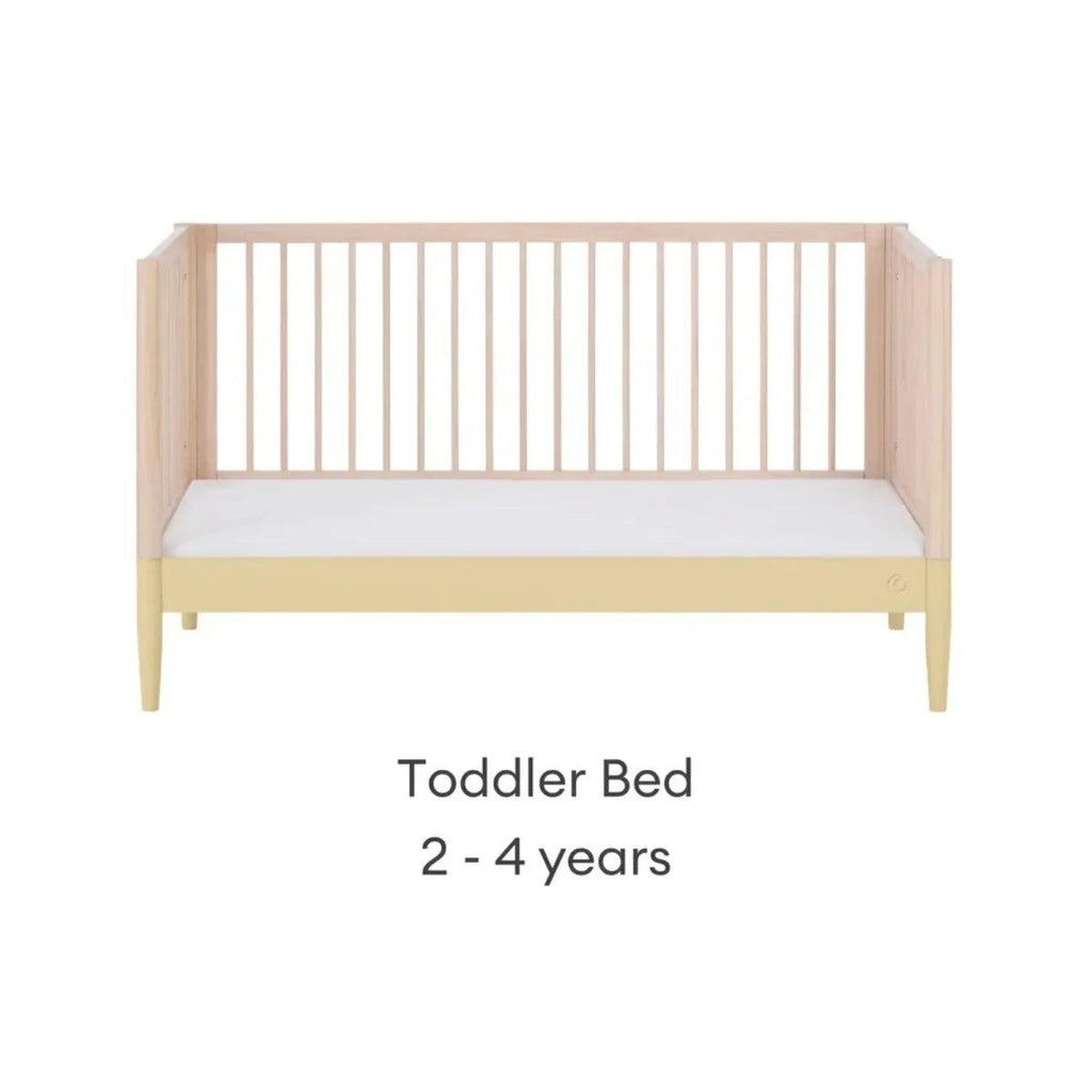 Convertible toddler bed with light wood frame and white mattress panel