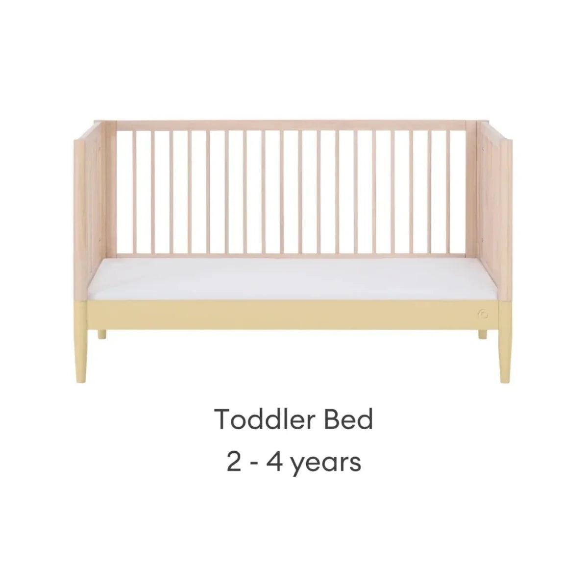 Convertible toddler bed with light wood frame and white mattress panel