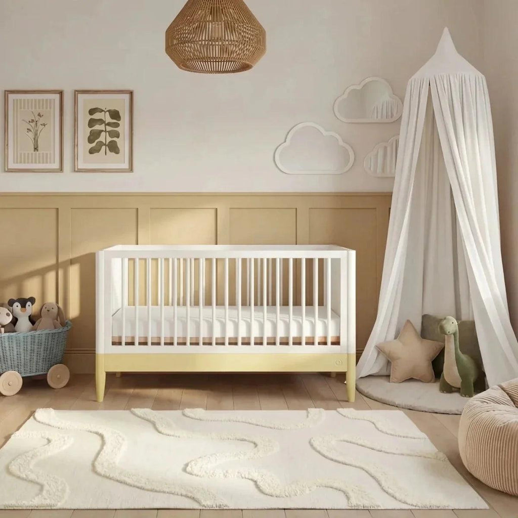 White baby cot bed with primrose yellow rail and draped white canopy