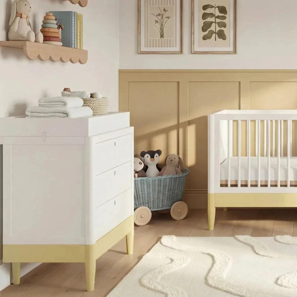 White baby cot bed with primrose yellow rail next to white storage cabinet