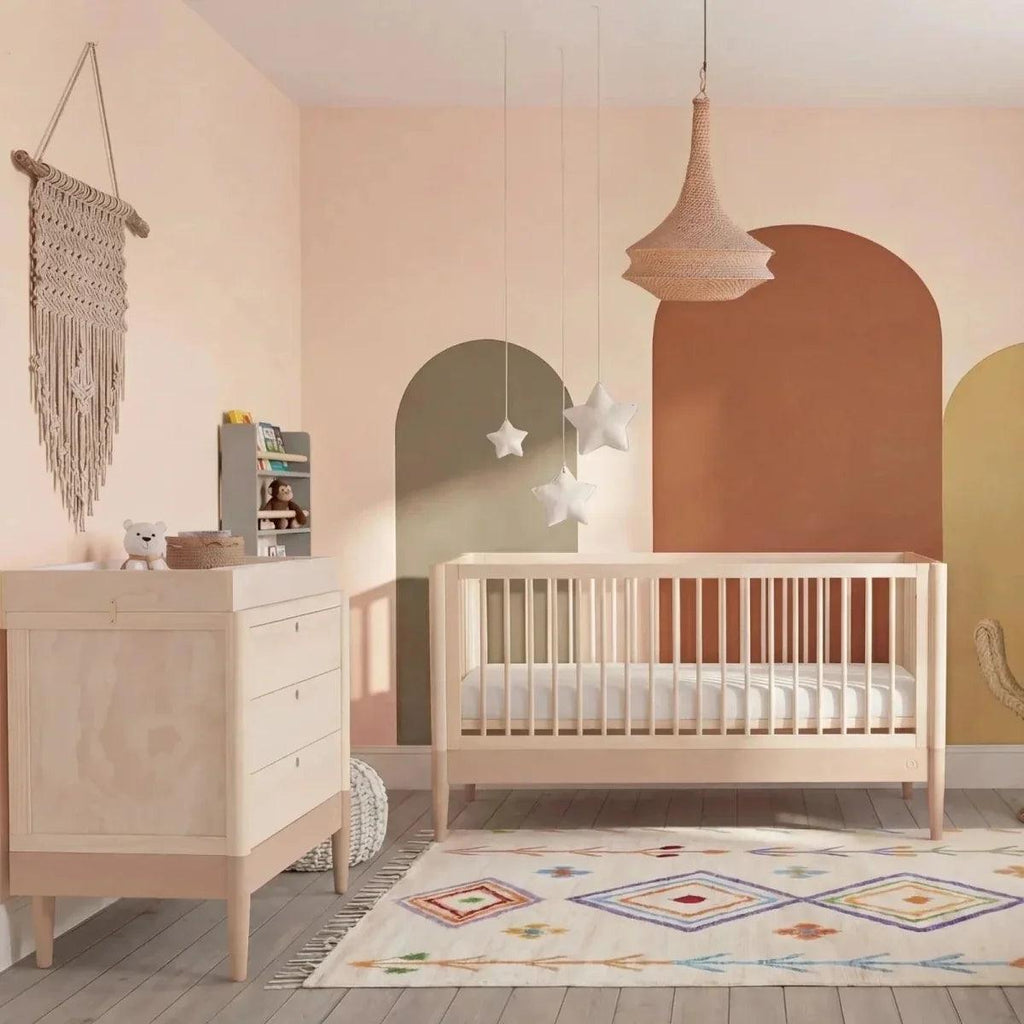 Light wood and white baby cot bed with tall headboard, in nursery styling