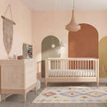 Light wood and white baby cot bed with tall headboard, in nursery styling