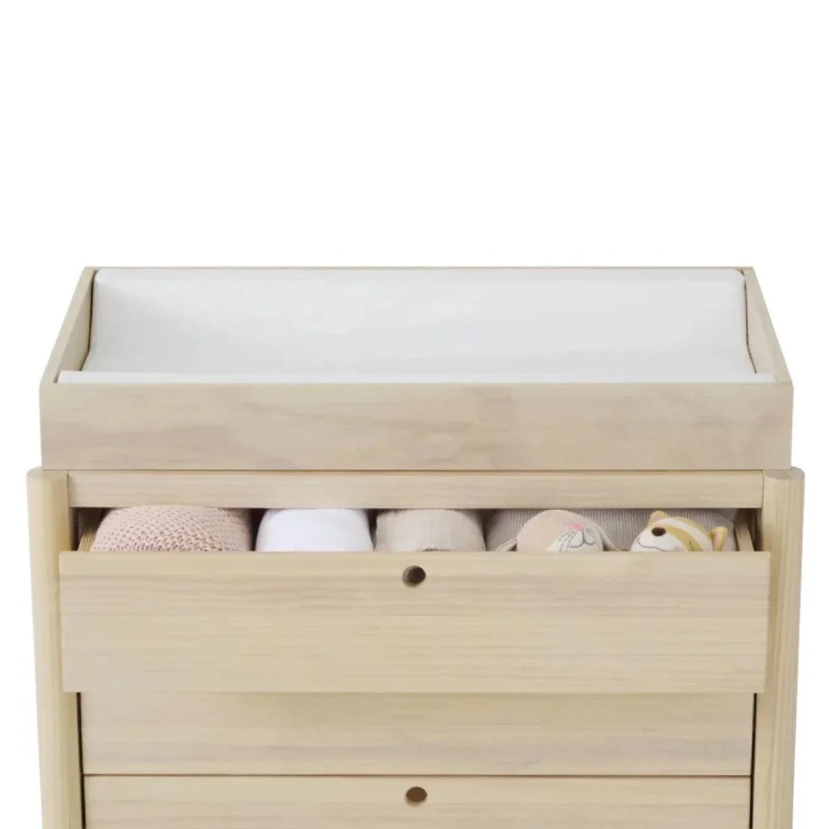 Baby changing chest with open storage drawer showing changing pad and small toys