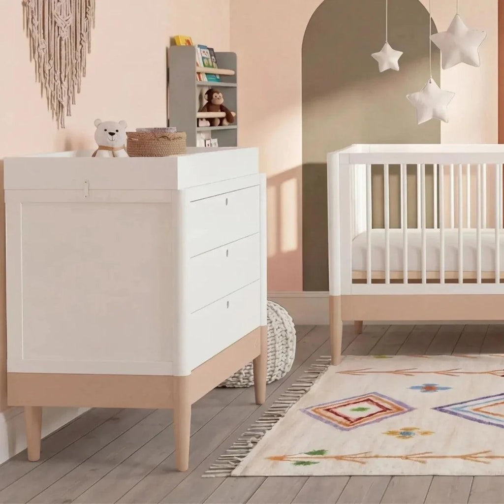 Powder blush and white baby room set with white crib beside matching dresser