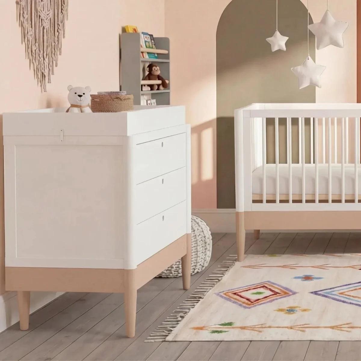 Powder blush and white baby room set with white crib beside matching dresser