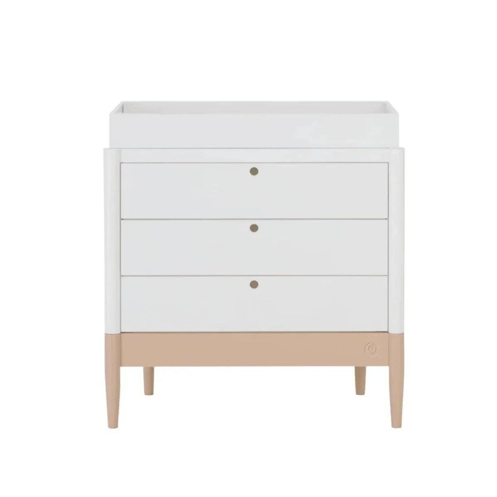 White dresser with three drawers, blush-toned base and tapered wooden legs