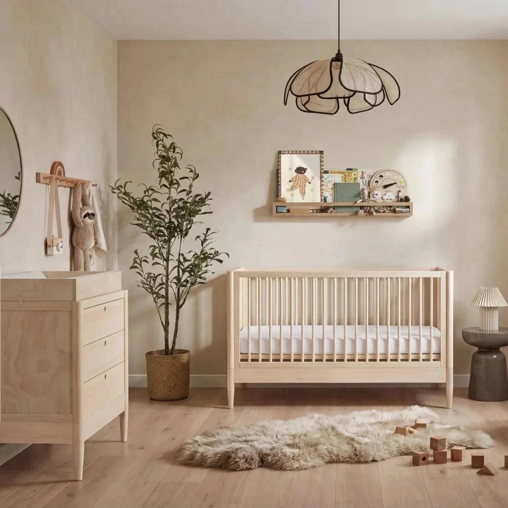 Natural ash nursery cot bed with slatted sides and white mattress platform