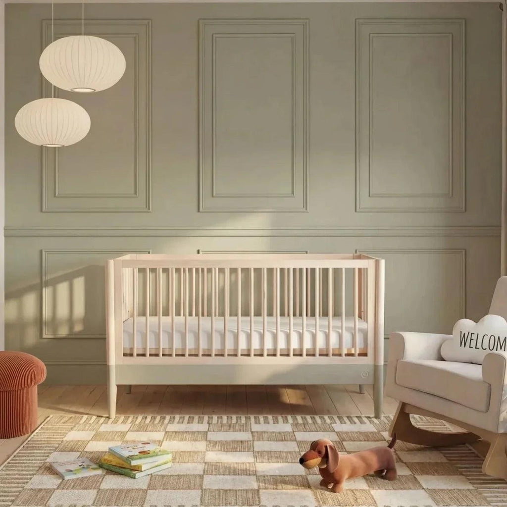 Baby cot bed with vertical slats, natural wood frame and desert sage accents, nursery view