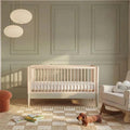 Baby cot bed with vertical slats, natural wood frame and desert sage accents, nursery view