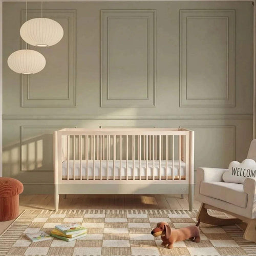 Baby cot bed with vertical slats, natural wood frame and desert sage accents, nursery view