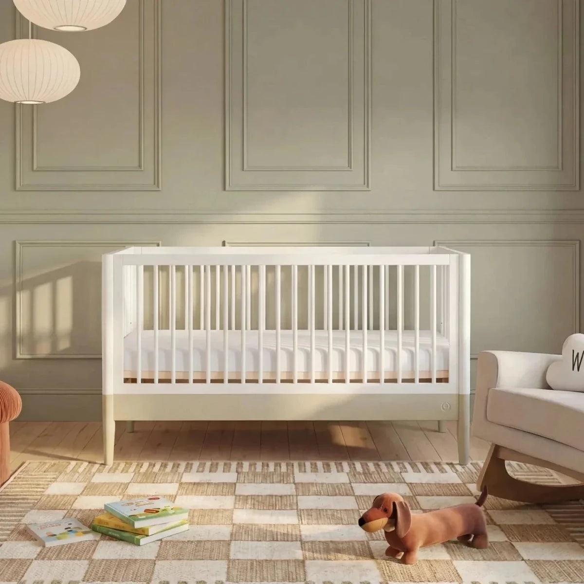 White baby cot bed with vertical slats and light wood legs, set in a nursery