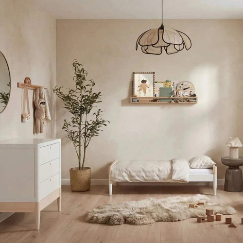 White baby cot bed with tall slatted sides and natural base in a nursery setting.