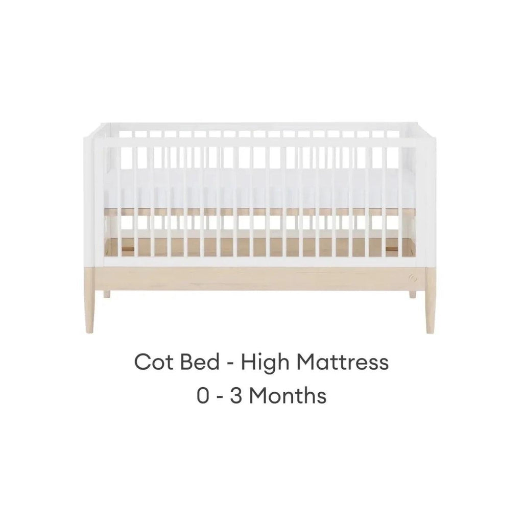 White cot bed with high mattress position, natural wood panel, and slatted rails.