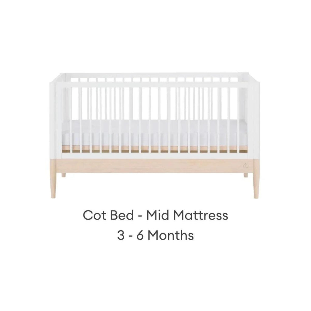 White cot bed with mid mattress position, natural wood panel, and vertical slat rails.
