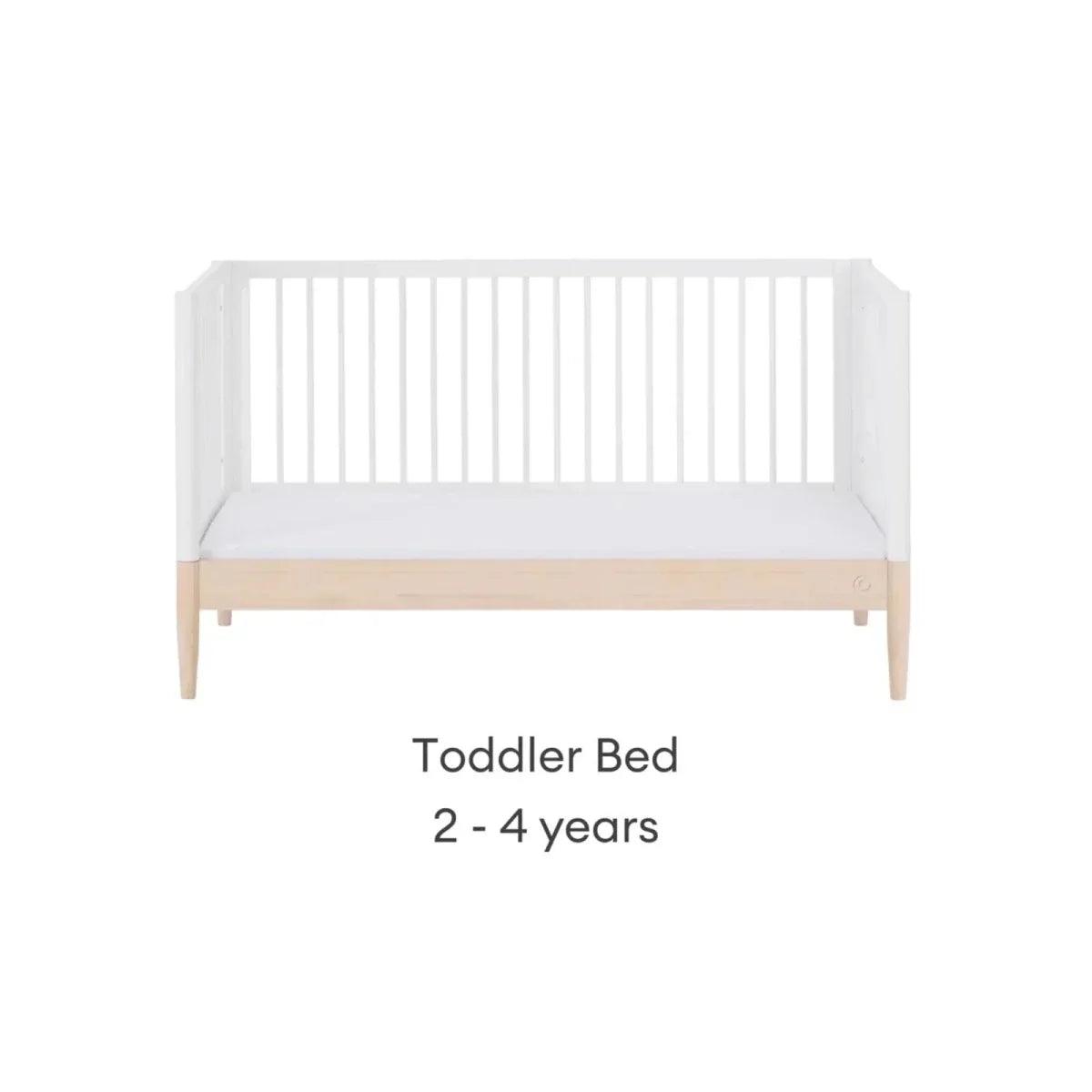 White toddler bed with low guard rails and natural wood base.