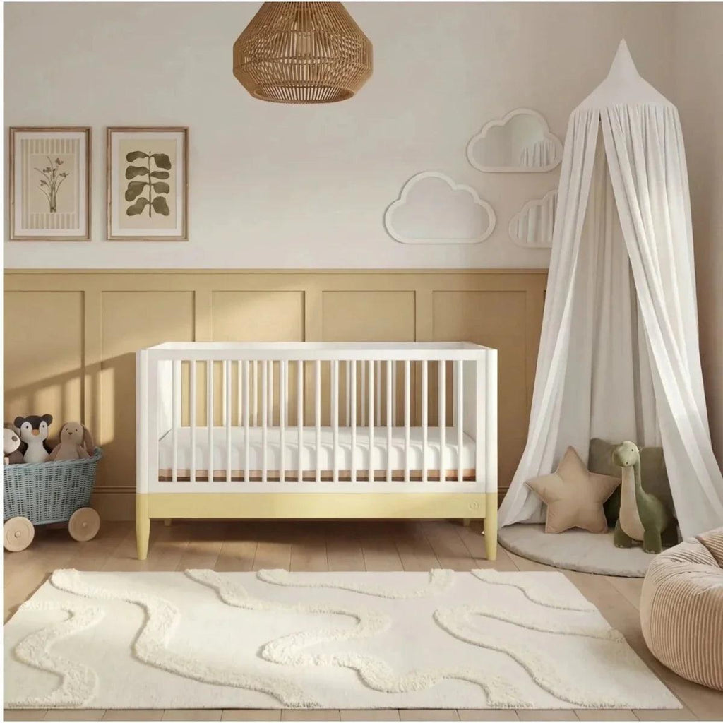 White and primrose yellow nursery cot bed with slatted rails and light wood legs