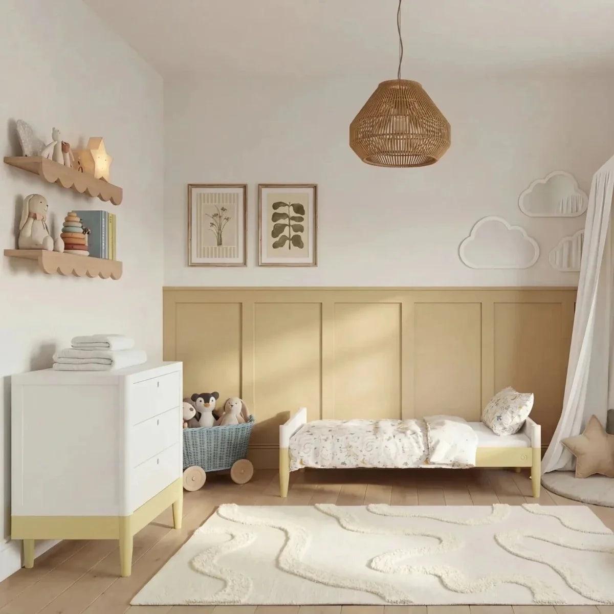 White nursery cot bed with primrose yellow rail, slatted sides, and light wood legs