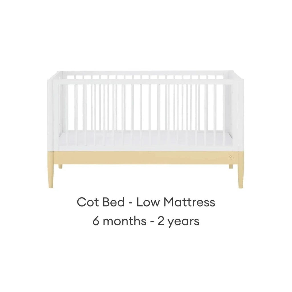 Cot bed with low-position white rails, primrose yellow trim, and pale wood legs