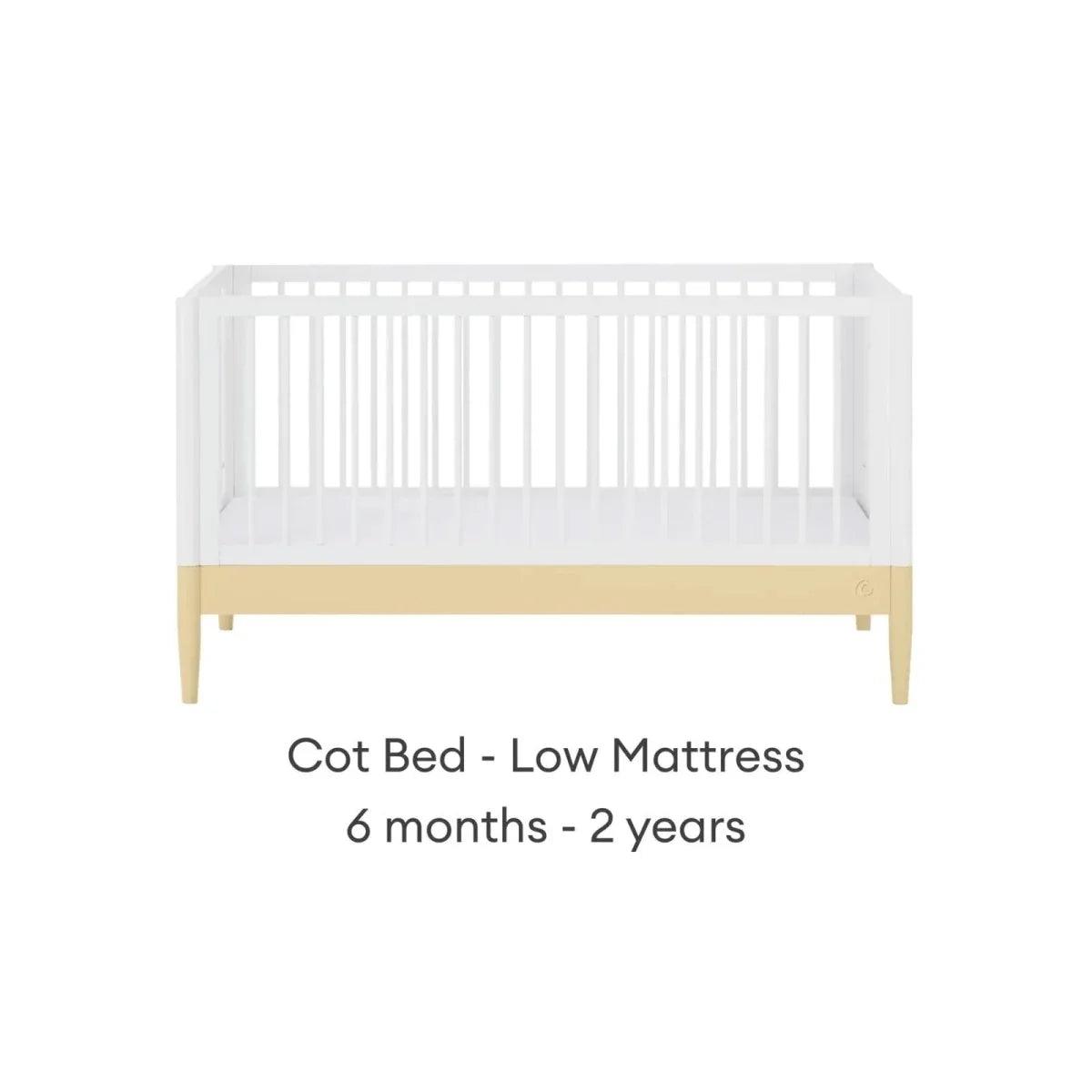 Cot bed with low-position white rails, primrose yellow trim, and pale wood legs