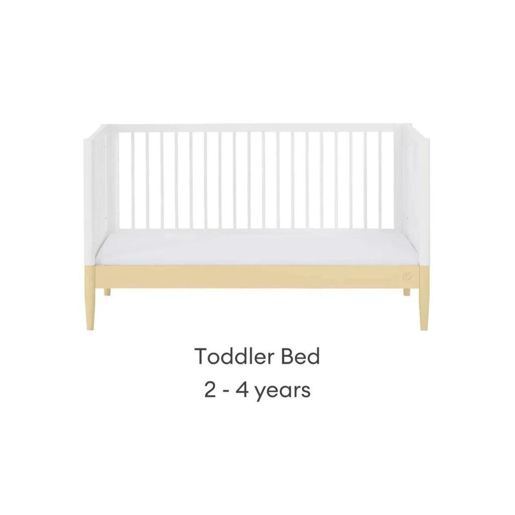 Toddler bed with white slatted sides and primrose yellow base trim, pale wood legs