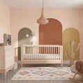 Nursery cot bed with powder blush frame and natural ash slatted sides, raised mattress.
