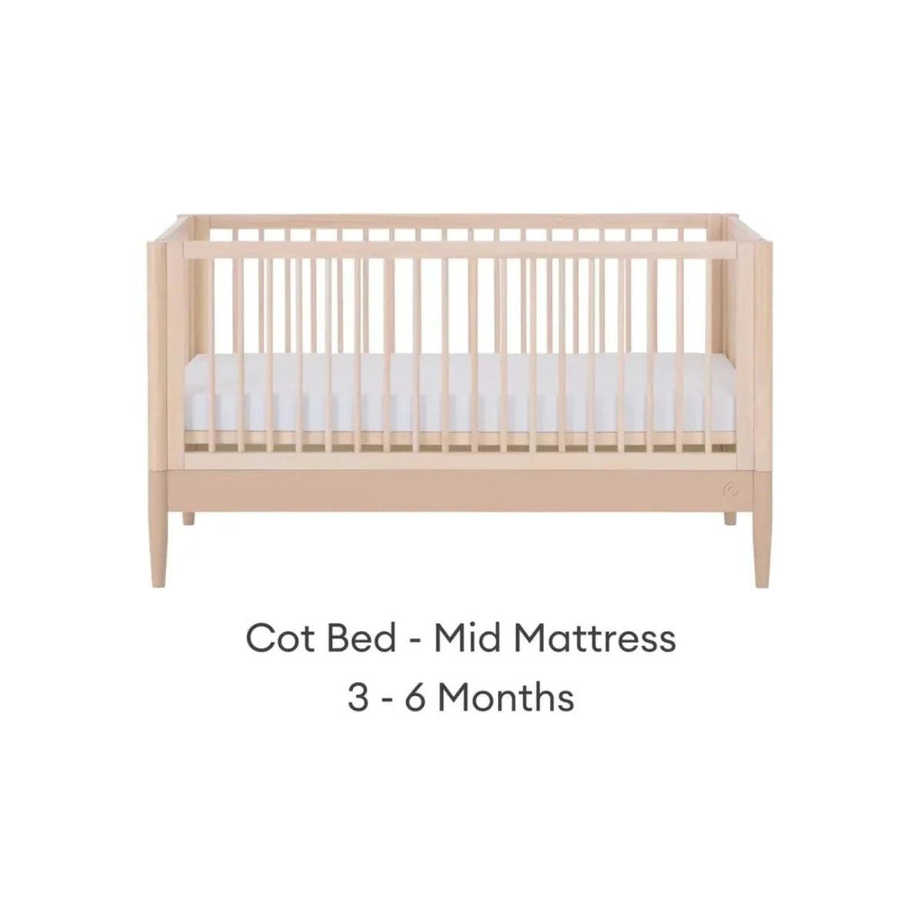 Cot bed with mid mattress position, natural ash frame and vertical slatted rails.