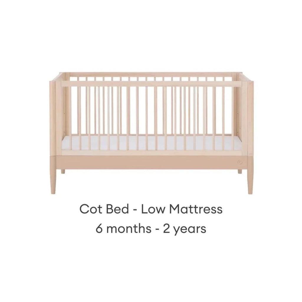Cot bed with low mattress position, natural ash frame and vertical slatted rails.