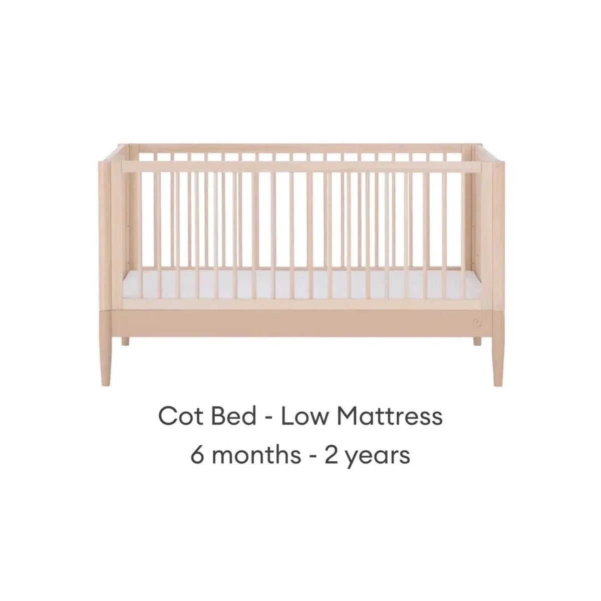 Cot bed with low mattress position, natural ash frame and vertical slatted rails.