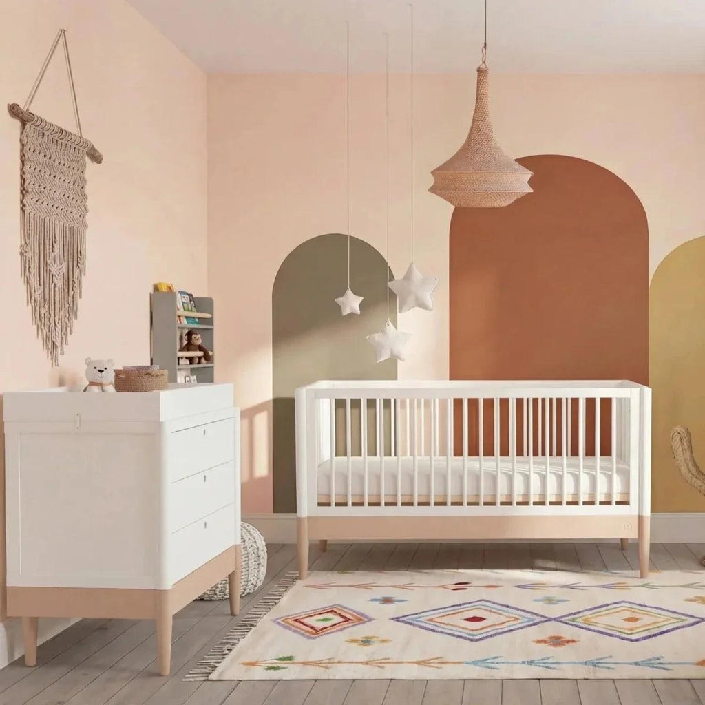 White cot bed with powder blush rails, open slats and light wooden legs