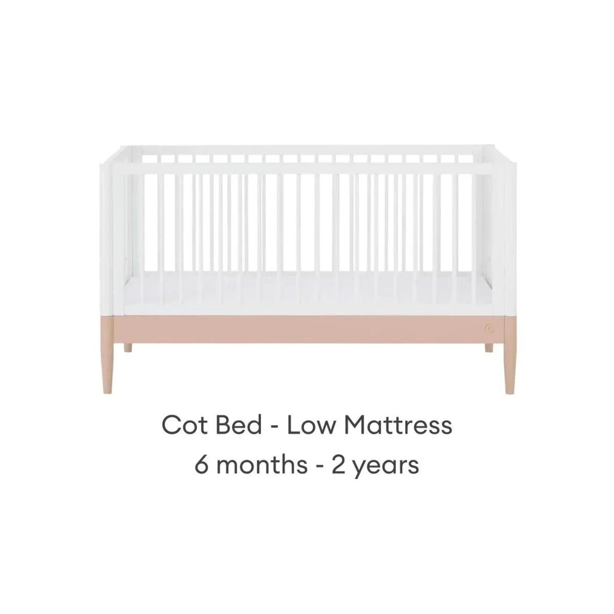 White cot bed with powder blush rail and vertical slats, low mattress position