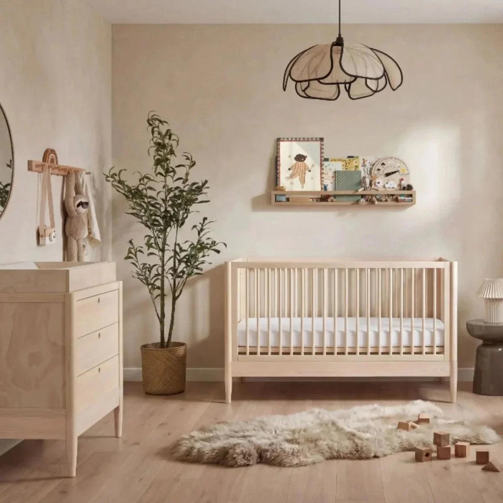 Light ash wood baby dresser with one visible drawer and round knob, flat top