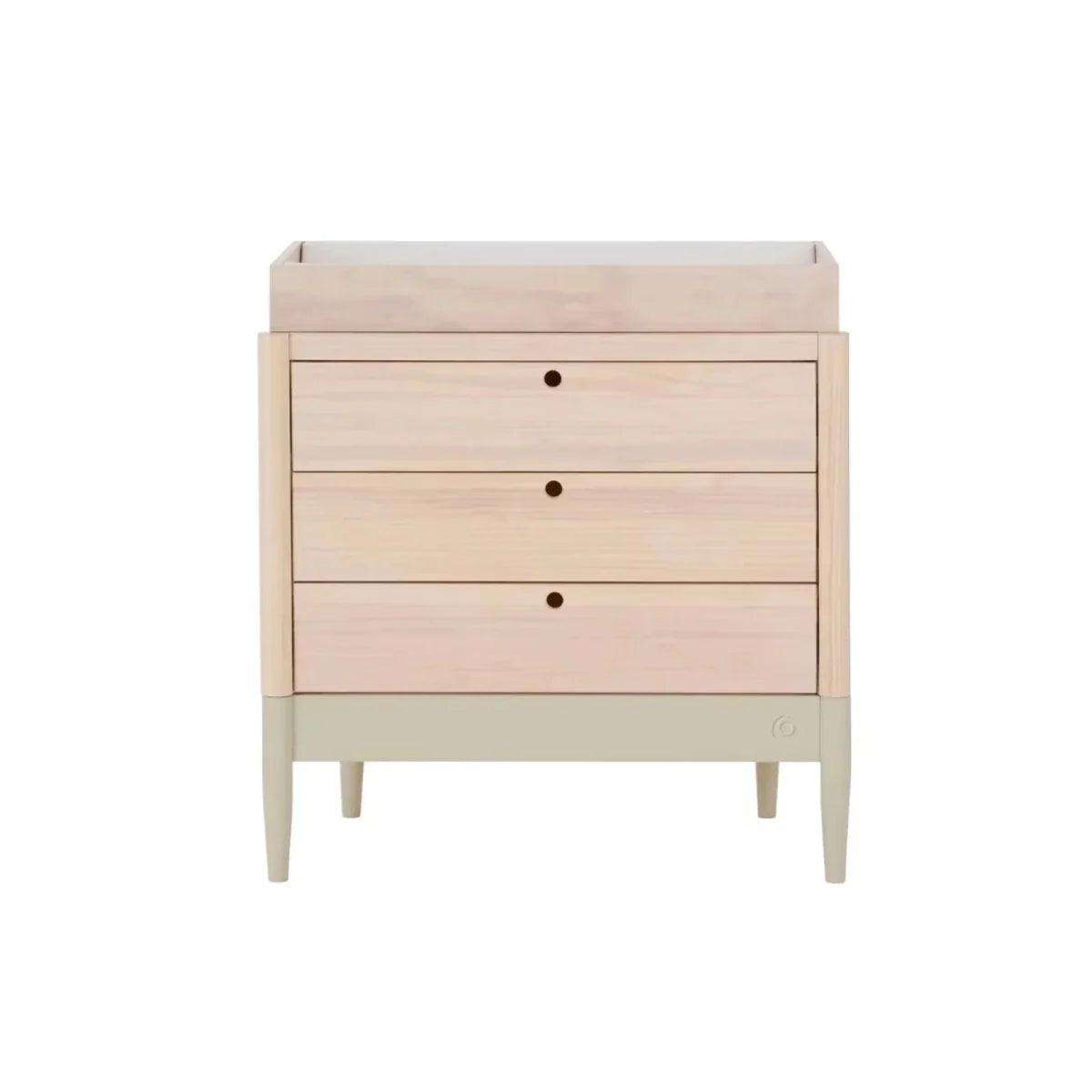 Light-wood baby dresser with three drawers, round dark knobs, and slim tapered legs