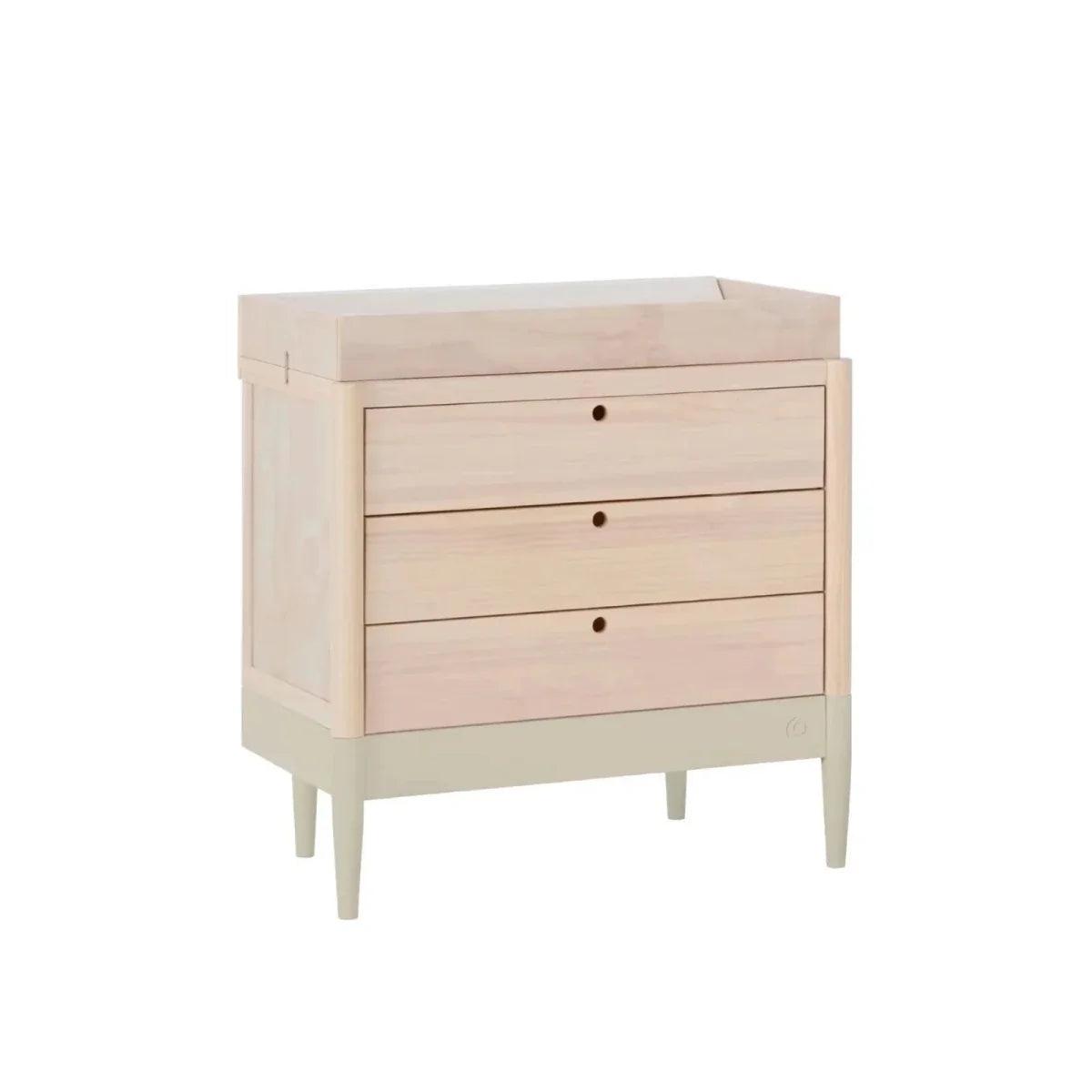 Light-wood baby dresser with three drawers, round knobs, and raised top edge