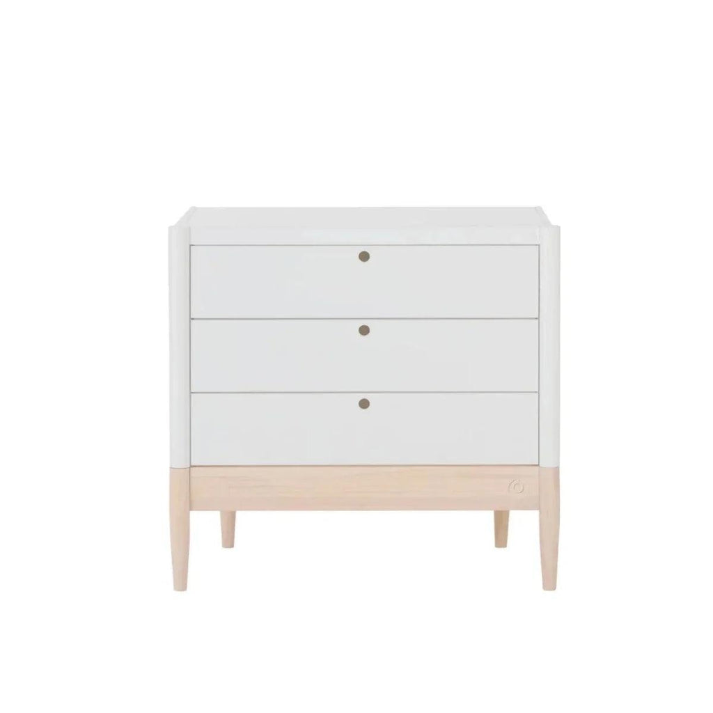 White baby dresser with three drawer fronts, round brass-tone pulls, and light wood base