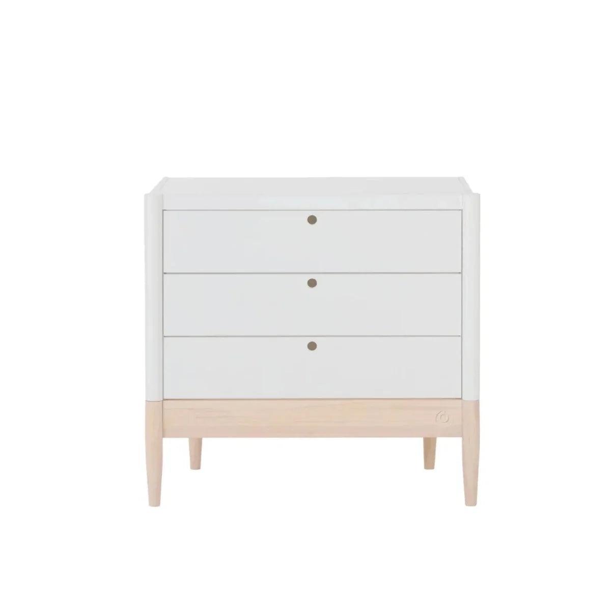 White baby dresser with three drawer fronts, round brass-tone pulls, and light wood base